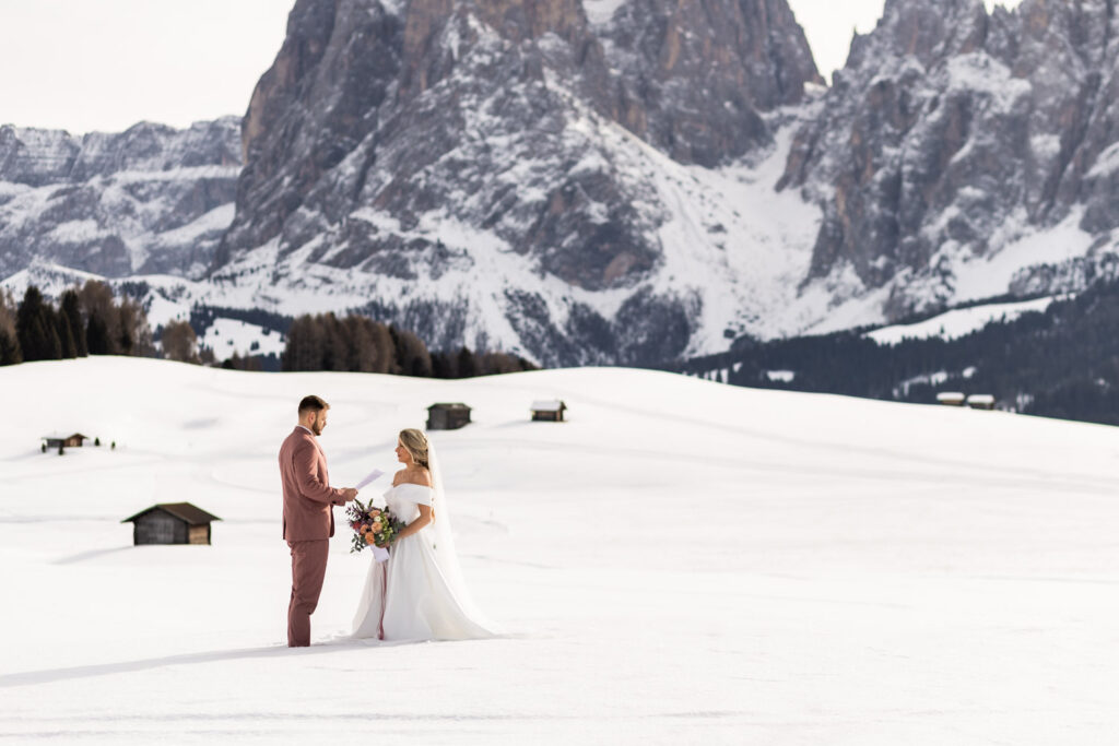 How to choose a photographer for your elopement? Couple standing on Alpe di Siusi mountain meadow doing their vows in winter.