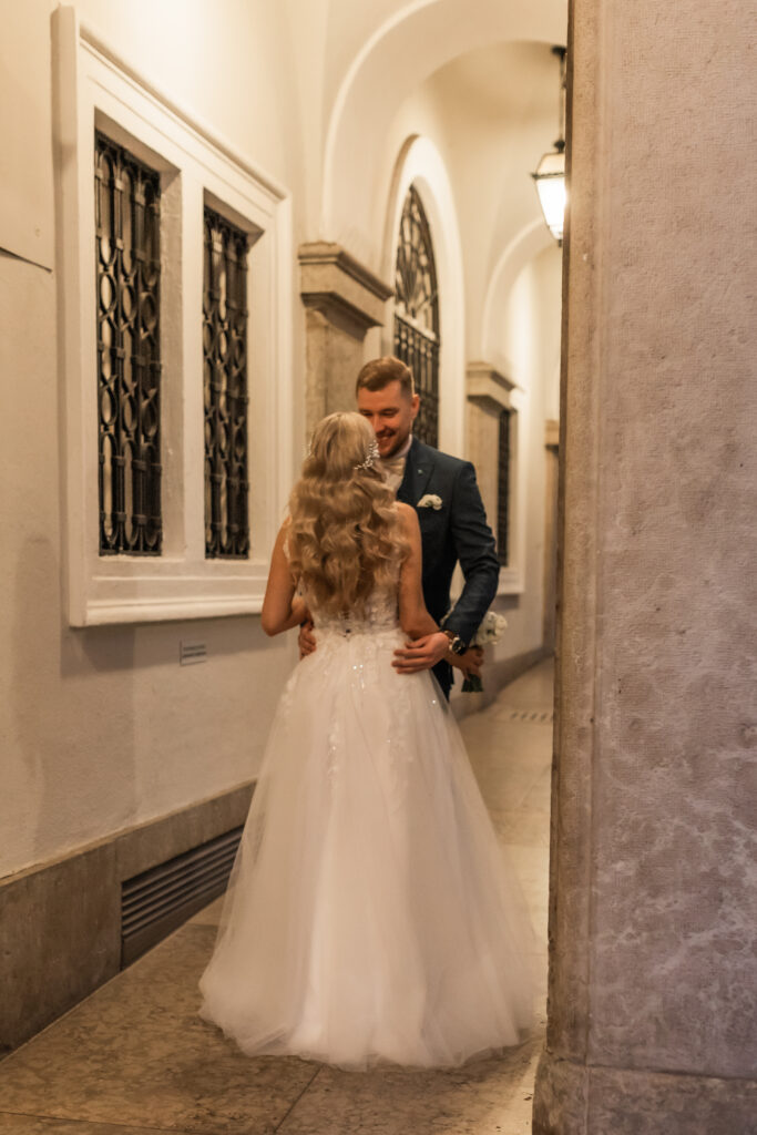 Romantic first look during an intimate Italy elopement, with bride in elegant white wedding dress and groom in dark suit, captured in a historic European hallway with soft lighting and arched architecture.