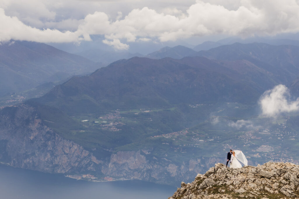 Couple standing on top of Monte Baldo at lake Garda in their wedding gown with majestic Alps as their background.