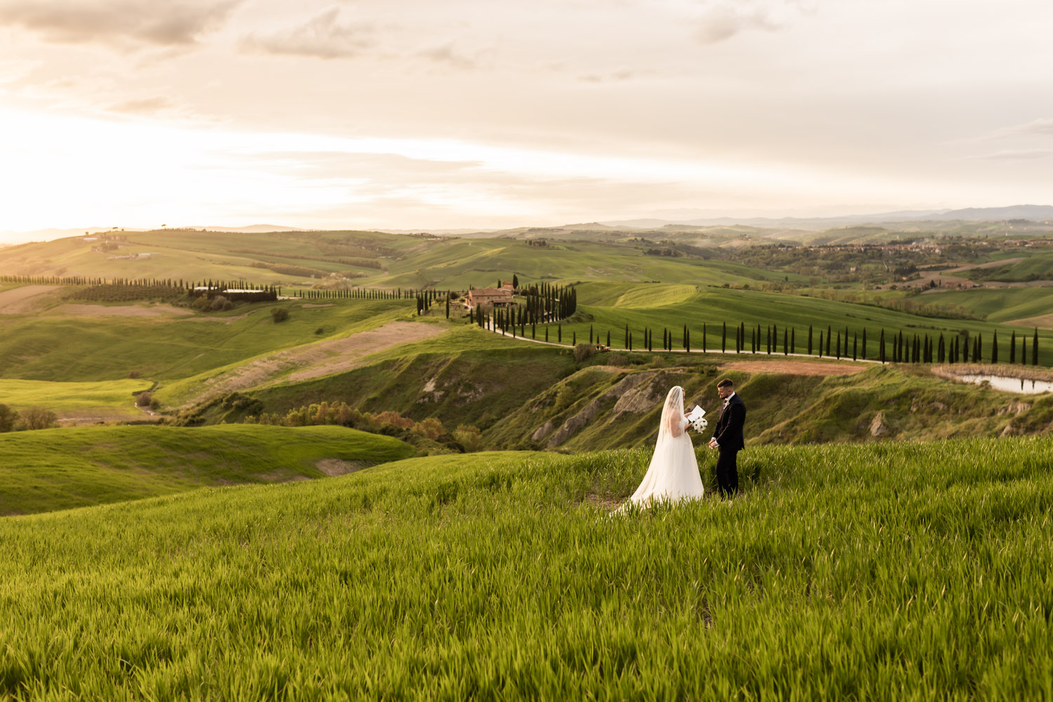Couple standing on Tuscany hills reading their vows to each other at sunset.