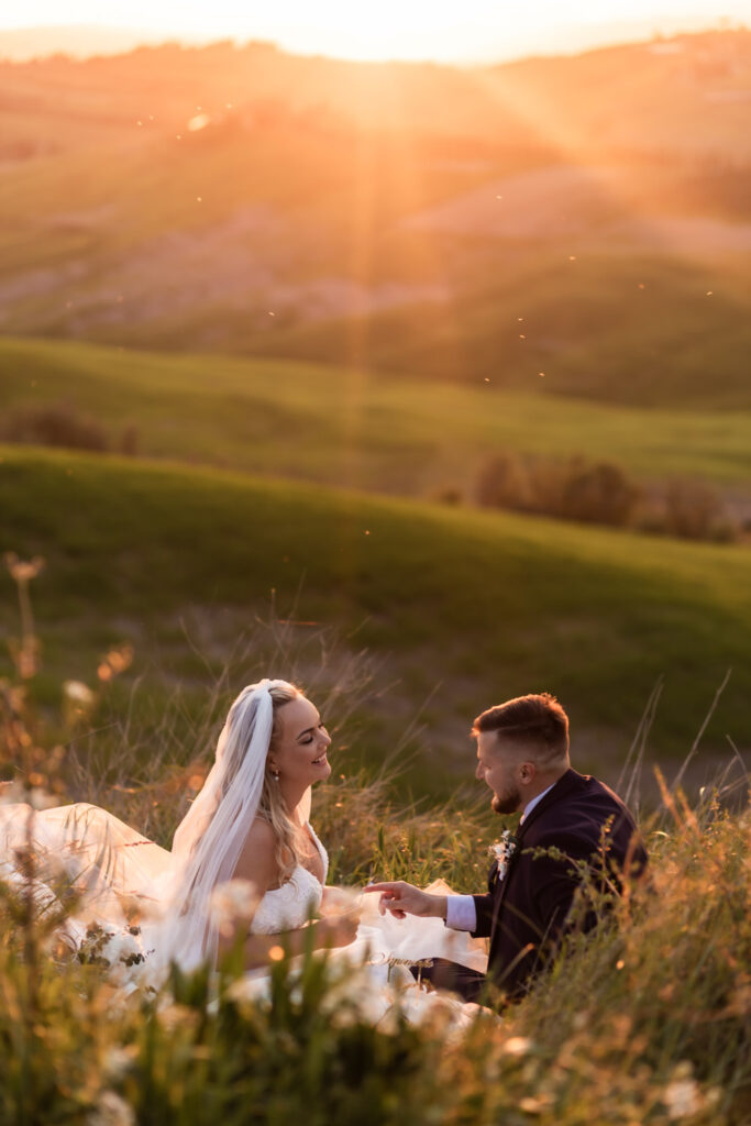 Couple having picnic and eating their wedding cake on Tuscany hills at sunset.