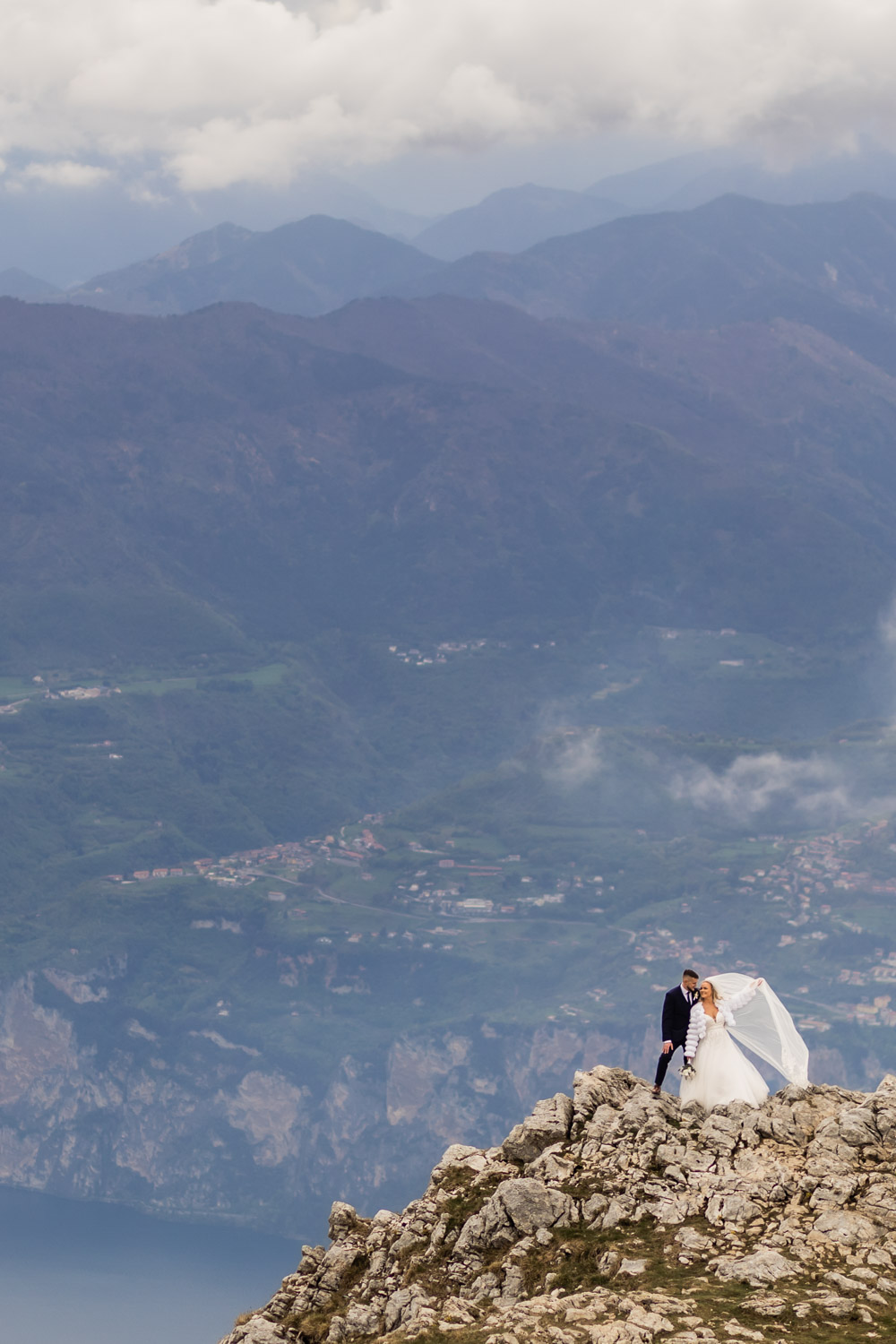 Couple standing on top of Monte Baldo at lake Garda in their wedding gown with majestic Alps as their background.