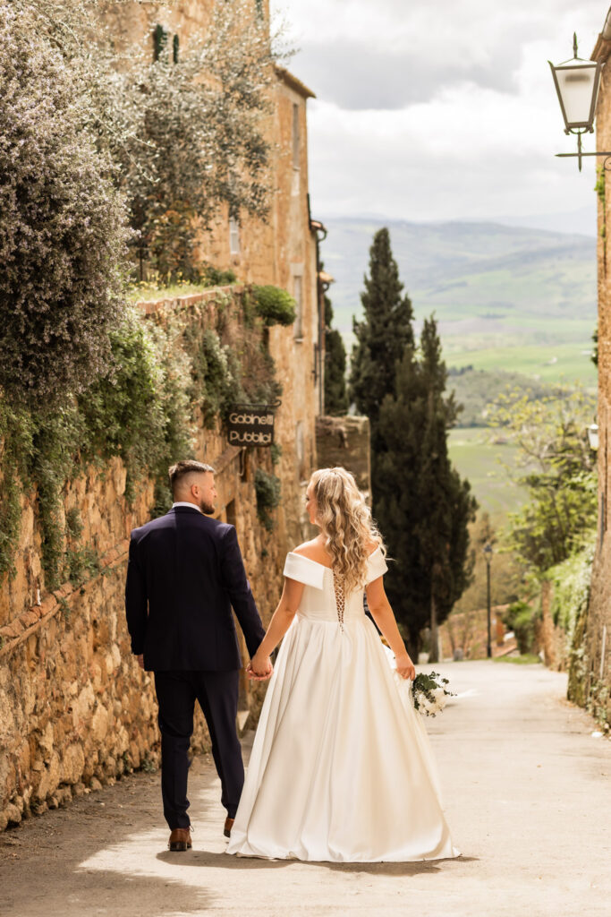 Husband and wife walking hand in hand in their wedding gown in a small Italian town.
