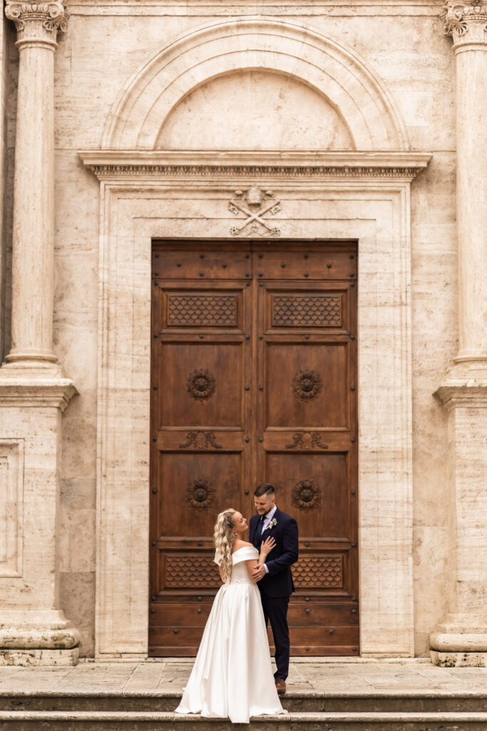 Husband and wife standing in their wedding gown in front of a big door in Italy