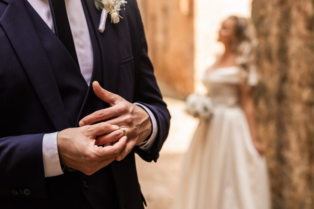 Close shot of husband putting on his ring, wife in wedding dress blurred on the background