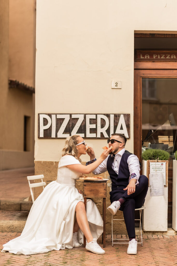 Husband and wife having pizza on their wedding day. They are in a little Italian town sitting in a pizzeria and having fun.