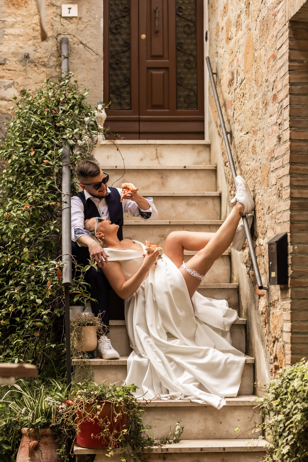 Husband and wife having pizza on their wedding day. They are in a little Italian town sitting on a staircase on the street and having fun.