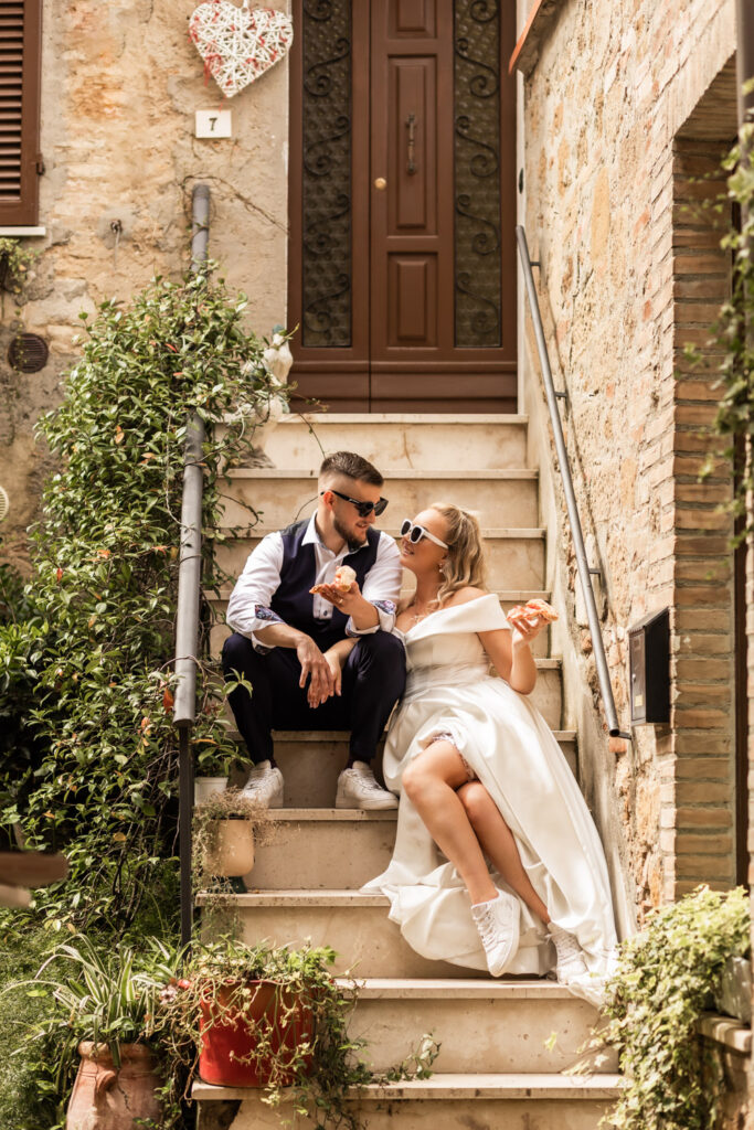 Husband and wife having pizza on their wedding day. They are in a little Italian town sitting on a staircase on the street and having fun.
