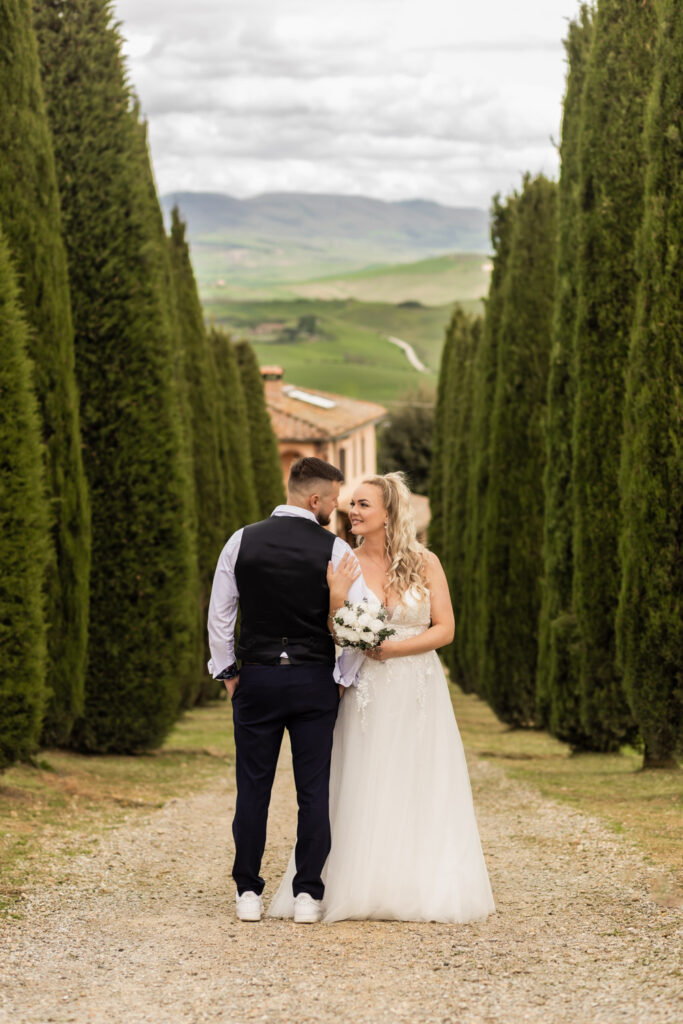 Husband and wife having a sweet moment in their wedding gown. They are standing in front of cypress trees in Tuscany.
