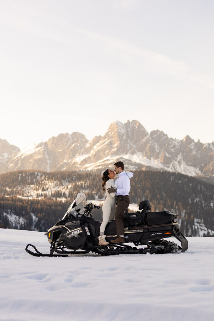 bride and groom hugging while standing on a snowmobile during their snowmobile elopement in Dolomites