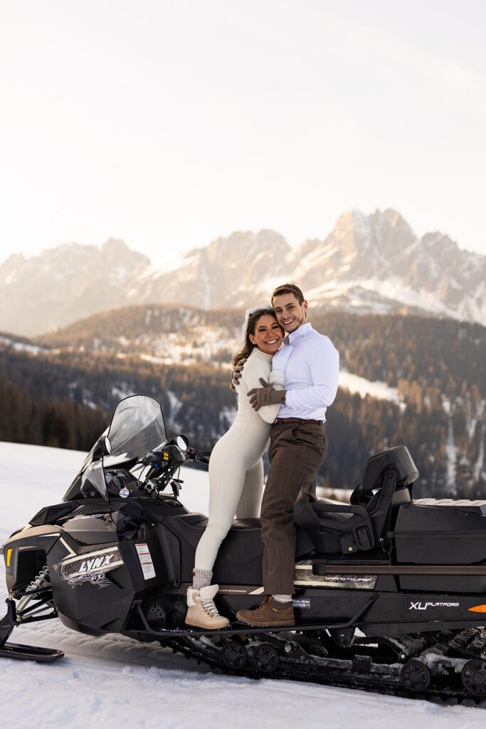 bride and groom hugging while standing on a snowmobile during their snowmobile elopement in Dolomites