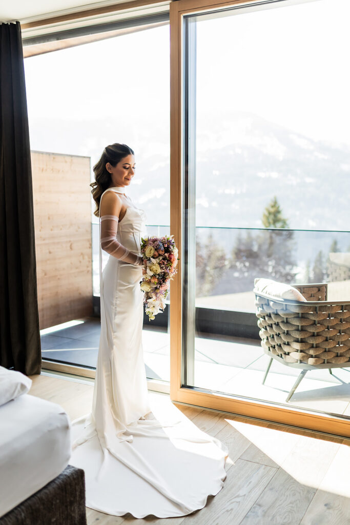 beautiful bride standing in front of the large window at the hotel with mountain views