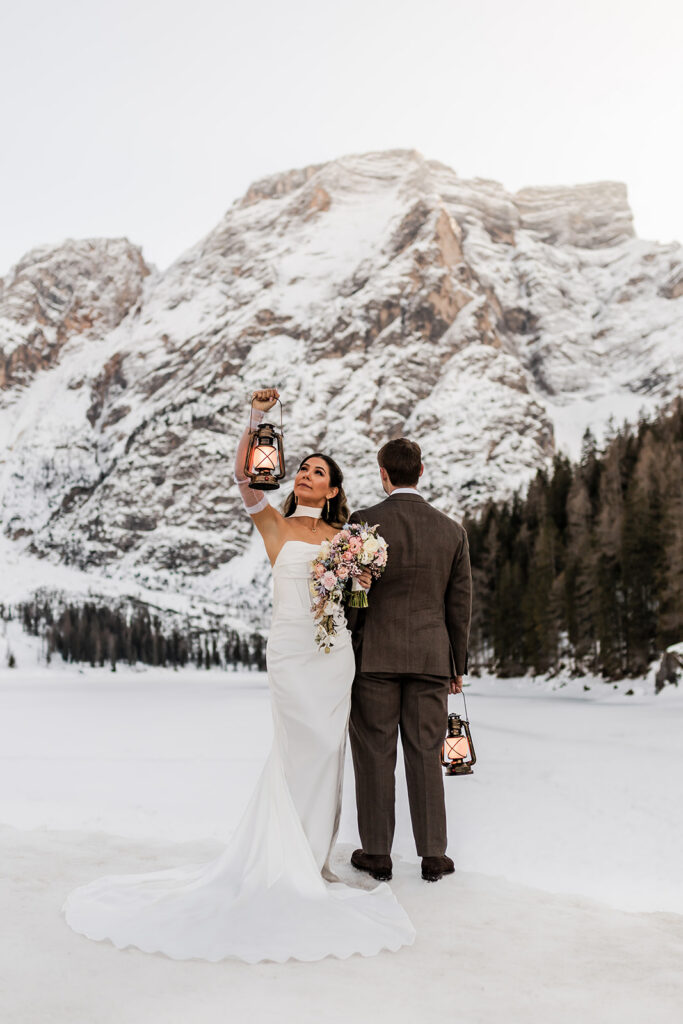 bride and groom posing with lanterns during blue hour at lake braies during their winter elopement in the dolomites