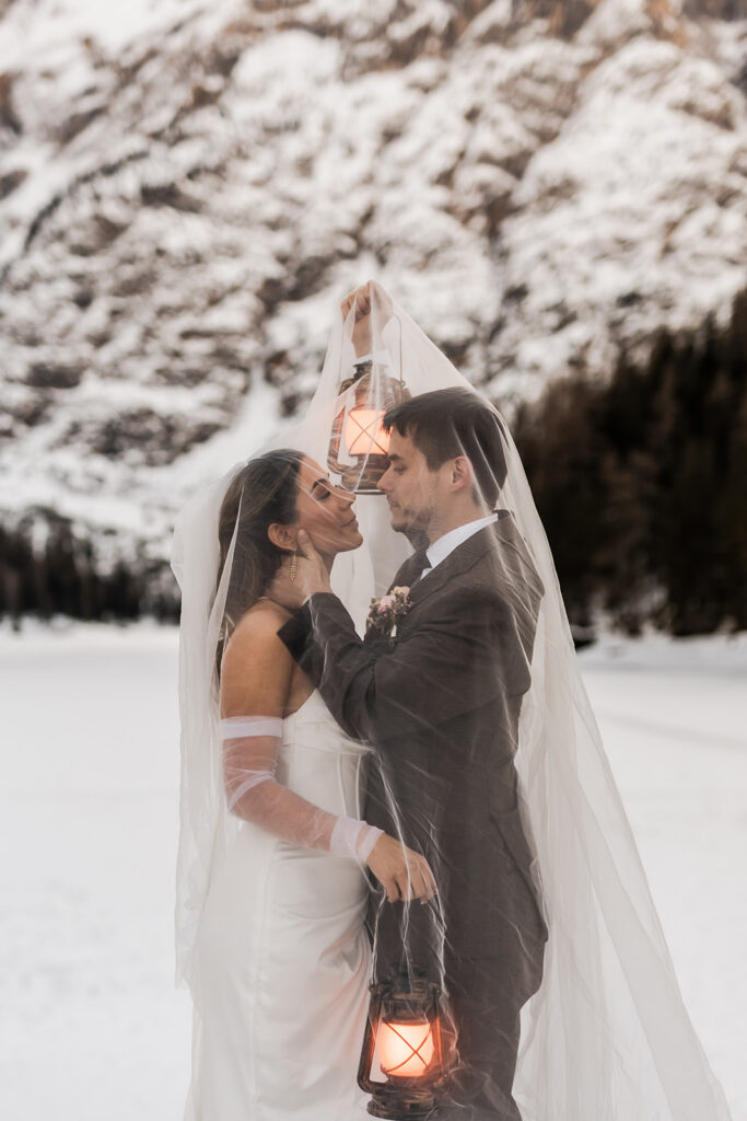 bride and groom posing with lanterns during blue hour at lake braies during their winter elopement in the dolomites