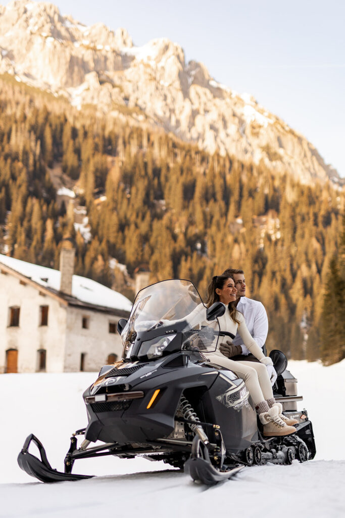 bride and groom sitting on a snowmobile and smiling during their snowmobile elopement in Dolomites