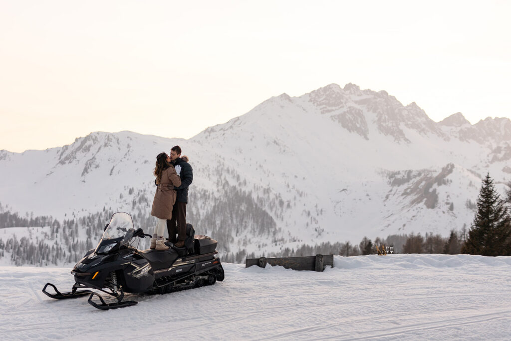 bride and groom hugging while standing on a snowmobile during their snowmobile elopement in Dolomites
