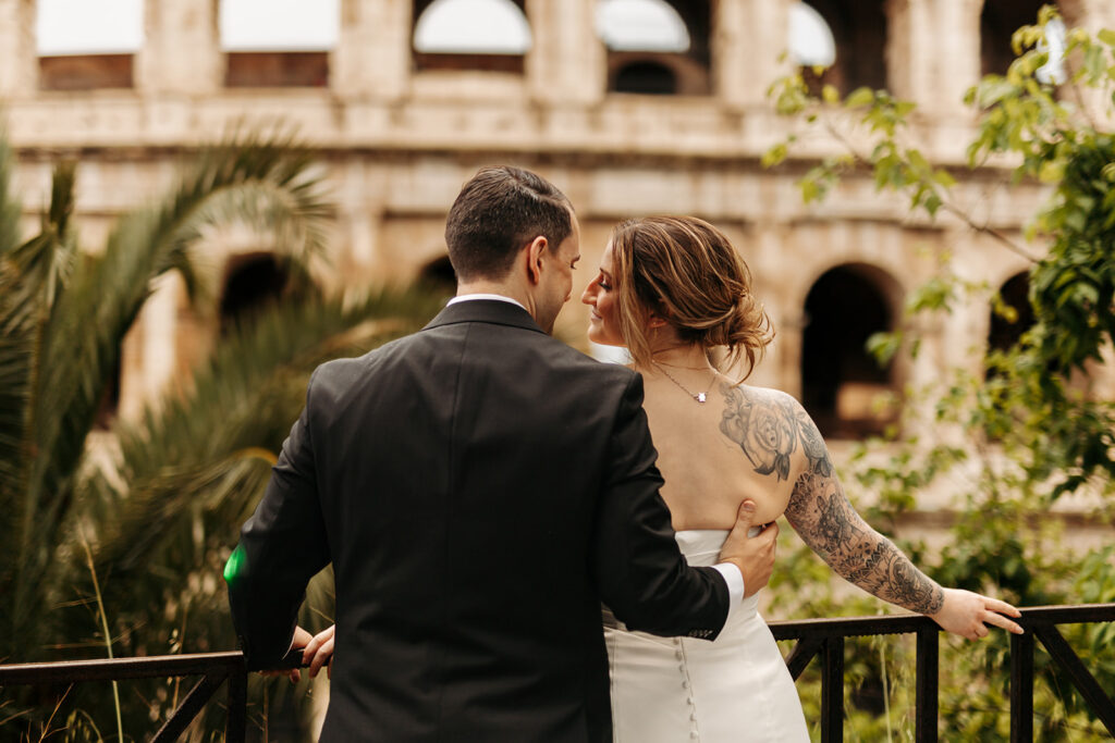 bride and groom standing in front of the coliseum in rome, italy