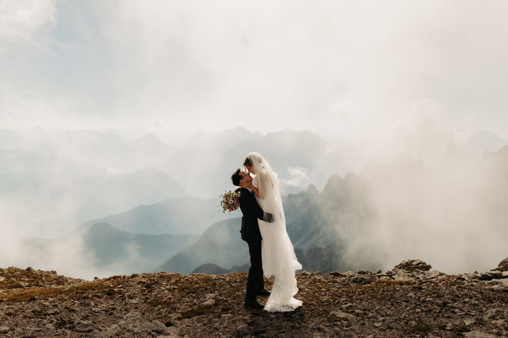 elopement couple kissing on a mountain top with clouds in the background