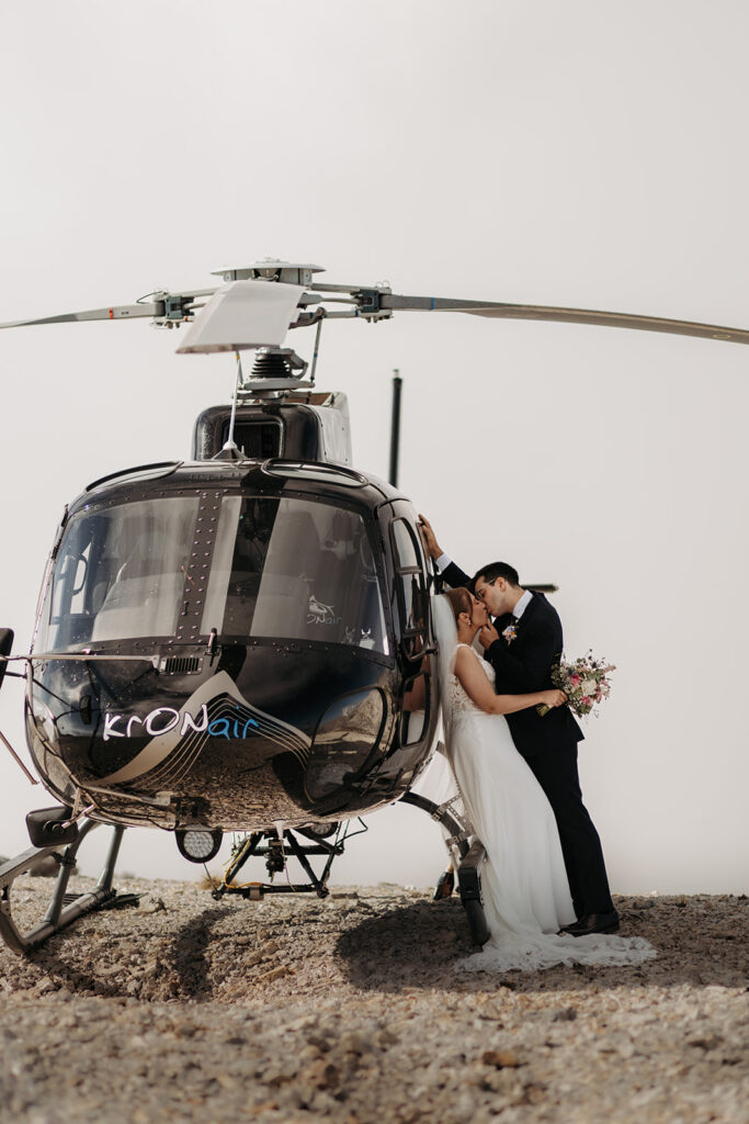 bride and groom kissing while leaning against a helicopter